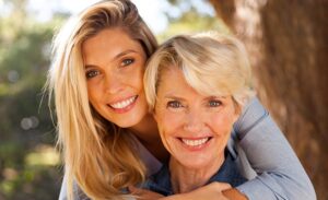 Photograph of a young woman with long blonde hair with her arms wrapped around an older woman with short blonde hair.
