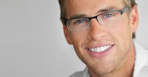 Photograph of an adult male smiling with white teeth, glasses and short blonde hair.