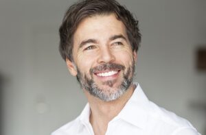 Photograph of a middle-aged man with a black and white beard and short black hair smiling and looking off into the distance.