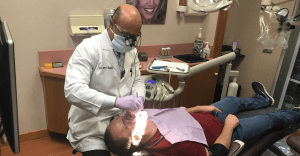 Dentist is wearing a mask while performing dental services on a patient as the patient is lying down in an office setting.